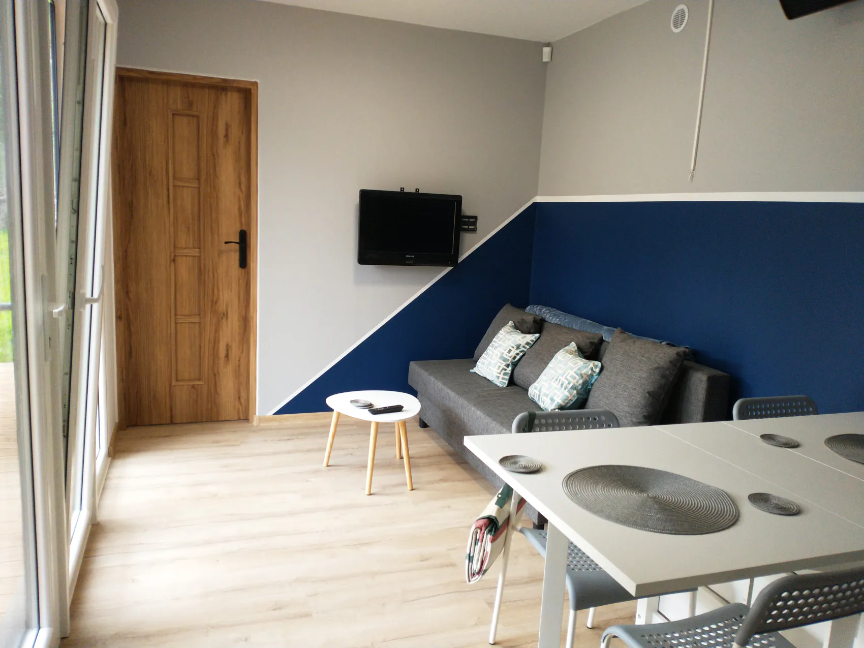 Helles Wohnzimmer mit Schlafsofa, TV und einer dunkelblauen Wand